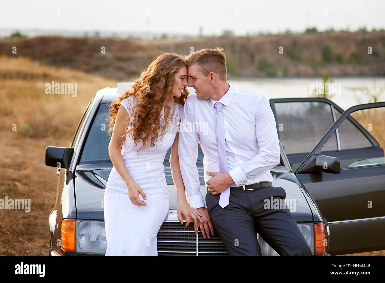 bride and groom sit on the hood of the car Stock Photo Alamy