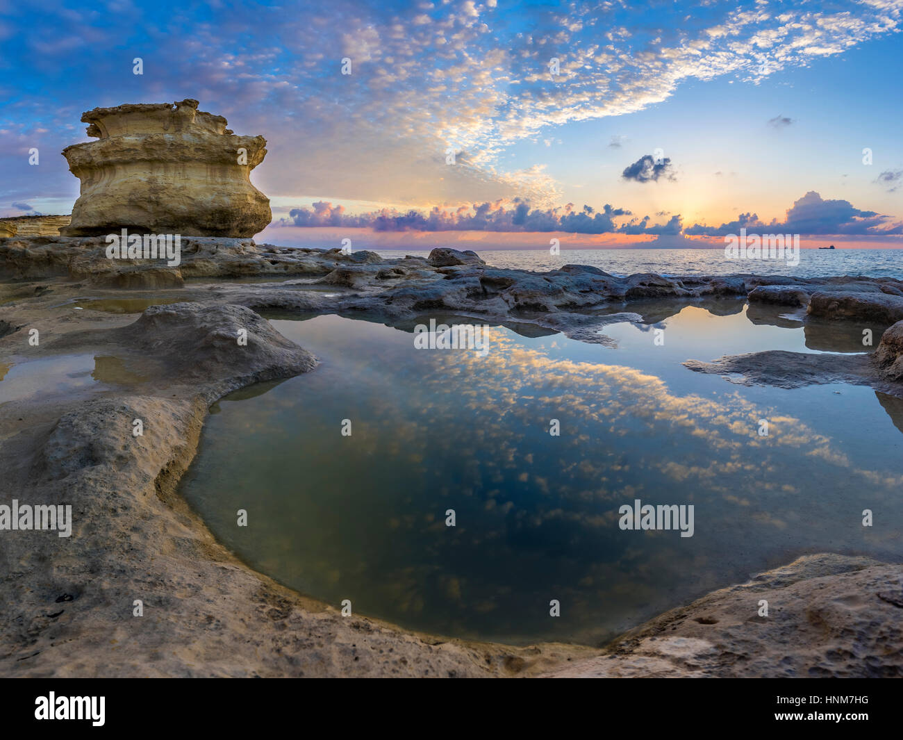 Malta - Sunrise at St.Peter's Pool with huge rocks of Delimara and reflections of the sky and clouds Stock Photo