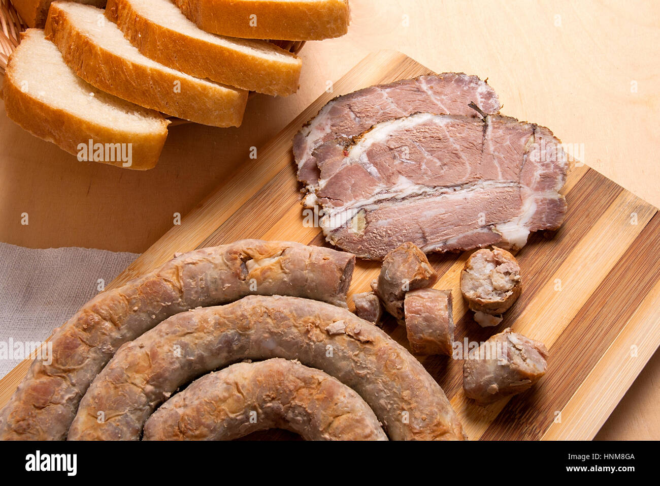 Roasted traditional homemade sausage with spices and herbs and slices spicy meat baked with herbs and spice on wooden cutting board. Slices white whea Stock Photo