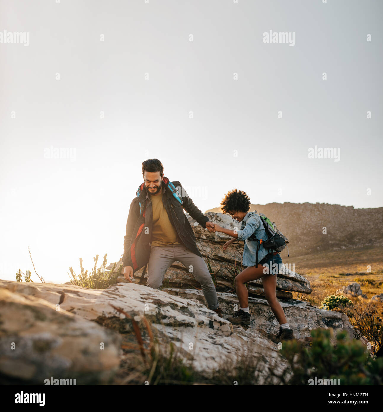 Young couple hiking help each other in mountains. Young male hiker