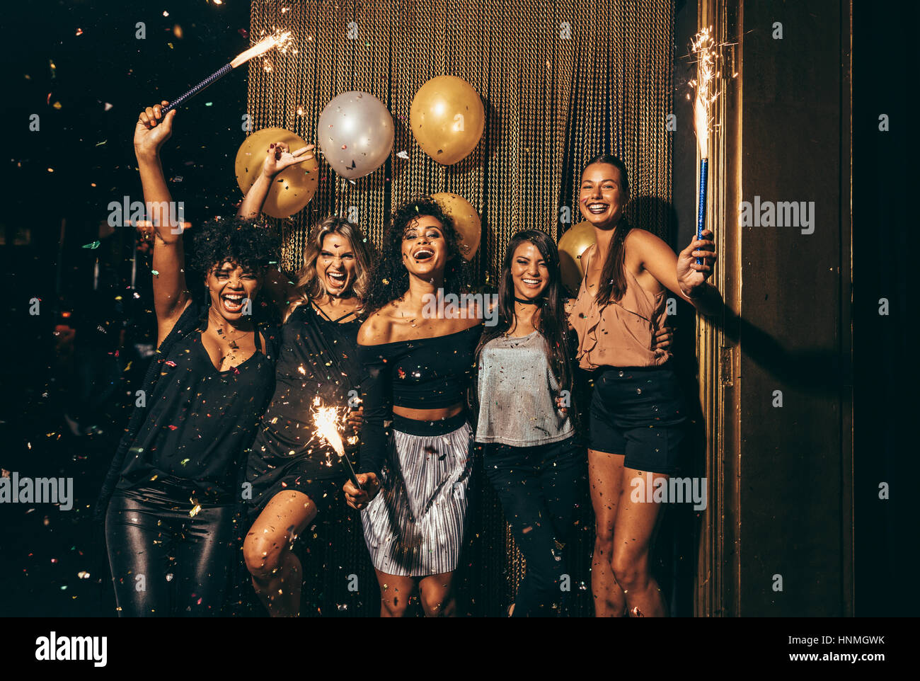 Shot best friends celebrating new year's eve holding sparklers in a party. Group of women having party at nightclub. Stock Photo