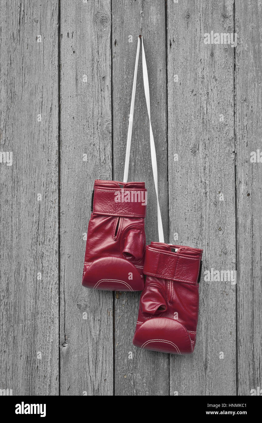 Red boxing leather gloves hangs on a nail, gray cracked wooden wall