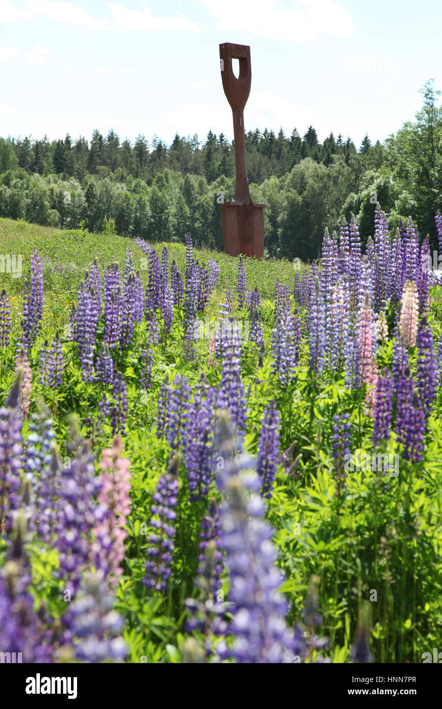 LUPINES in meadow with a sculpture of a shovel at HÃ¤lleforsnÃ¤s,an old industrial center in SÃ¶rmland with manufacturing industries Stock Photo