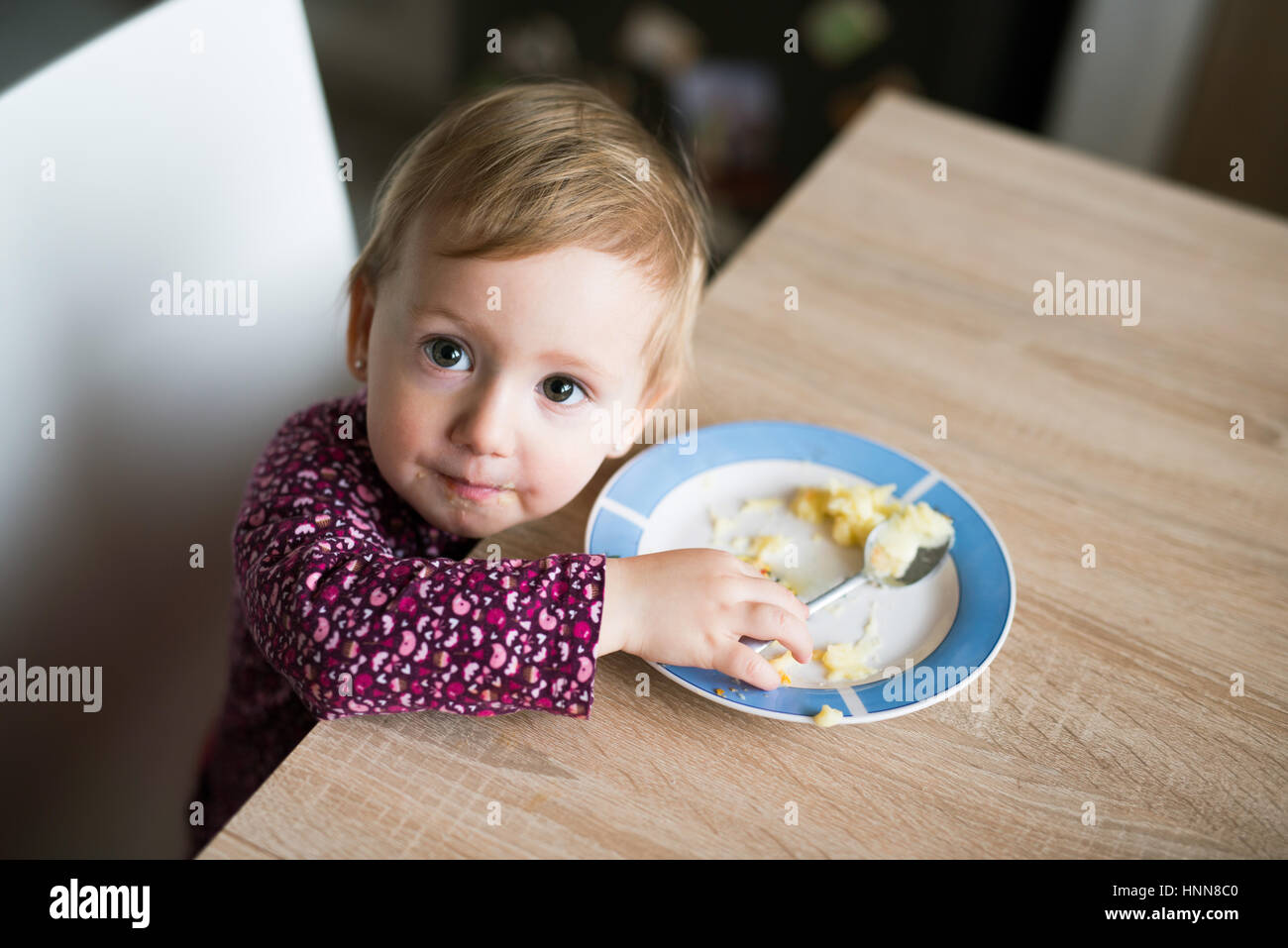 Cute little girl sitting at the table eating mashed potatoes Stock Photo