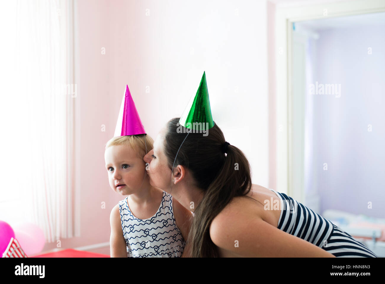 Beautiful mother kissing her cute daughter wearing party hats Stock Photo