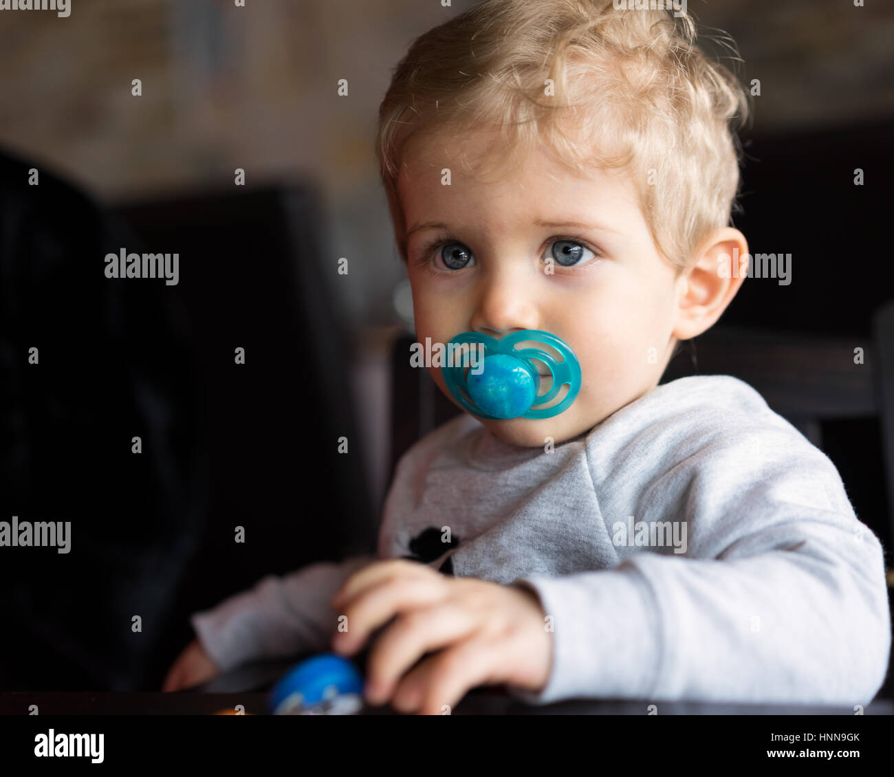Baby boy sitting in high chair and thoughtful with pacifier at chinese ...