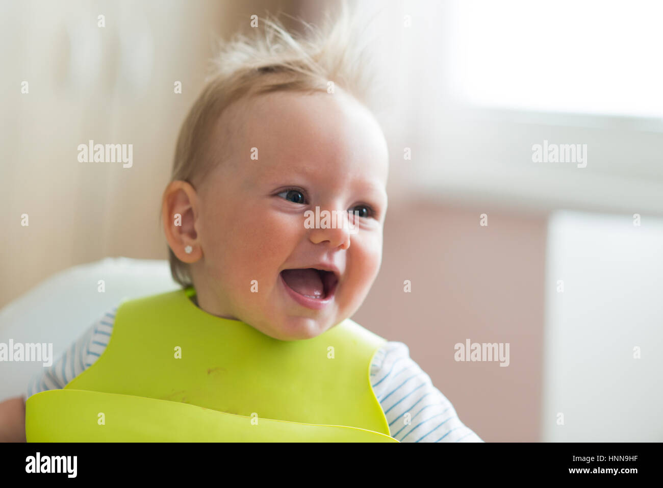 Cute little girl with bib sitting in high chair laughing Stock Photo Alamy