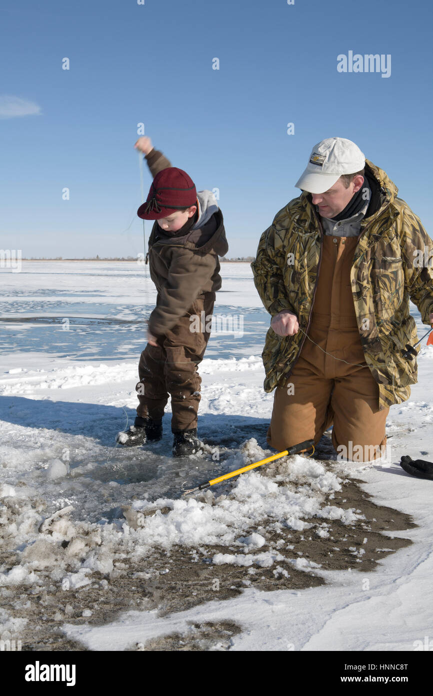 A boy frantically pulls in line while a man watches after a northern pike hit a minnow, ice