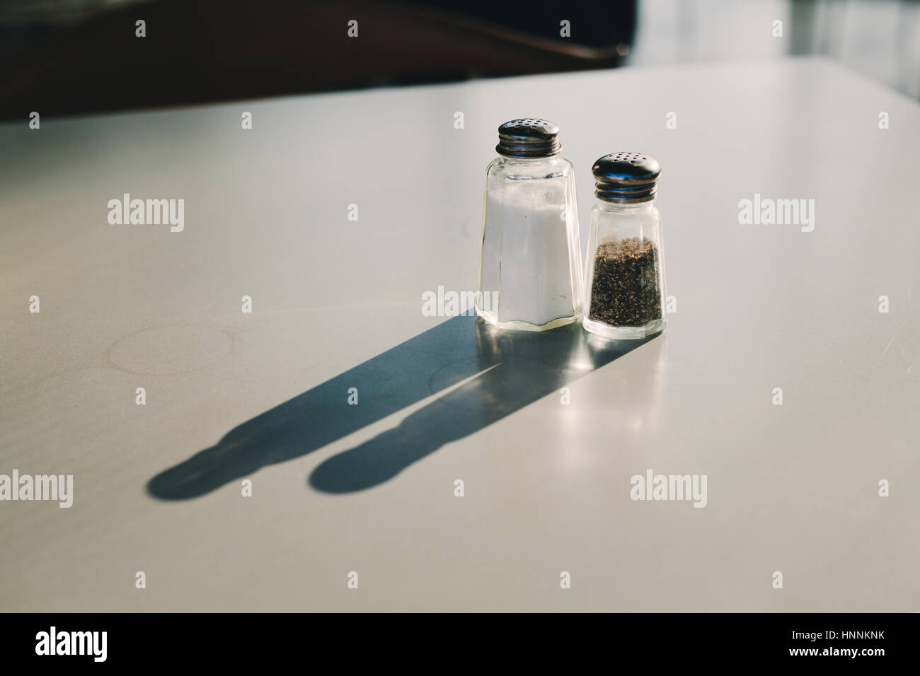 Sunlit salt & pepper on a table casting a long shadow Stock Photo