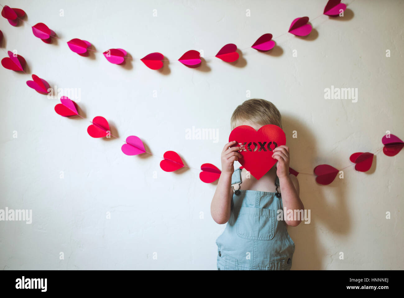 Boy hiding face with heart shape while standing against wall Stock Photo