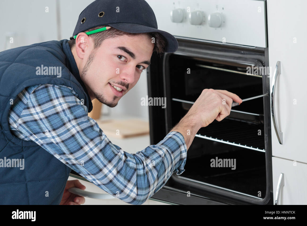 young repairman in overall installing brand new oven in kitchen Stock