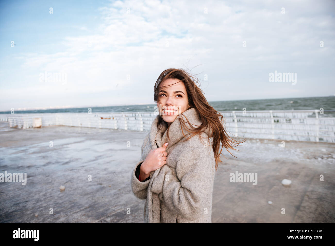 Happy beautiful young woman standing and smiling on pier in winter Stock Photo
