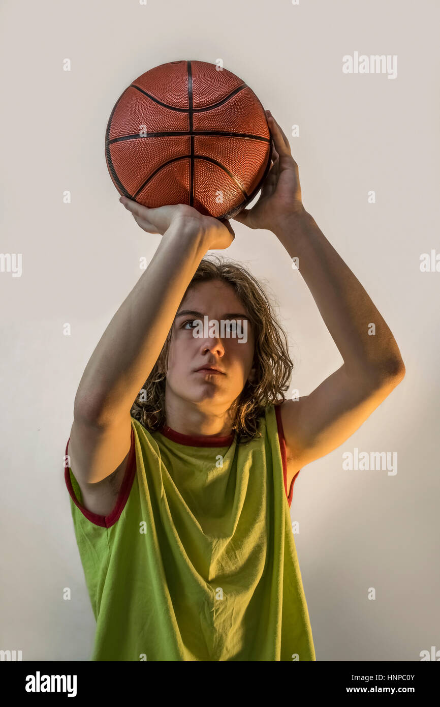 Young boy with blond hair and a green jersey on playing basketball focusing on throwing the ball. Stock Photo
