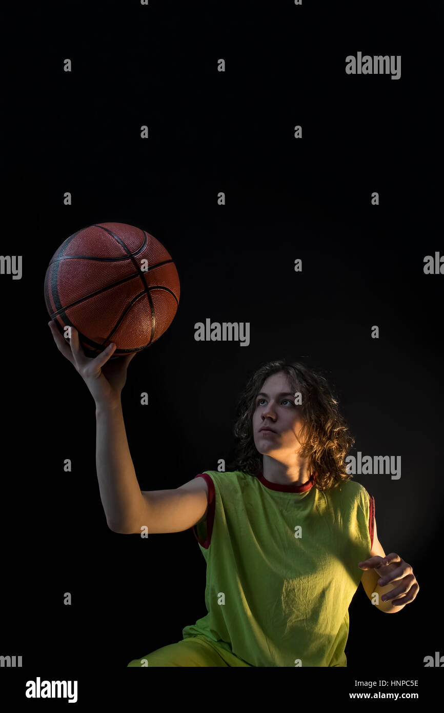 Young boy with long blond hair wearing a green jersey looking determinedly at the basket ball. Stock Photo