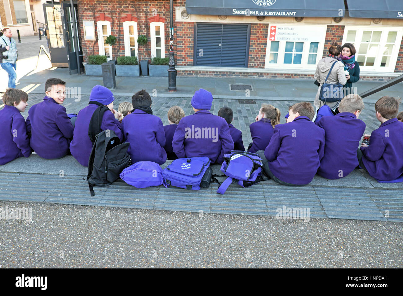 Rear view of a group of primary school children in purple uniforms sitting near the Globe Theatre on Bankside in South London UK  KATHY DEWITT Stock Photo