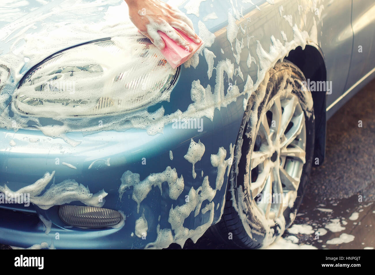 Washing the car by hand with soapy sponge. Cleaning the car. Car care concept. Hand of man washing the car using the sponge with foam Stock Photo