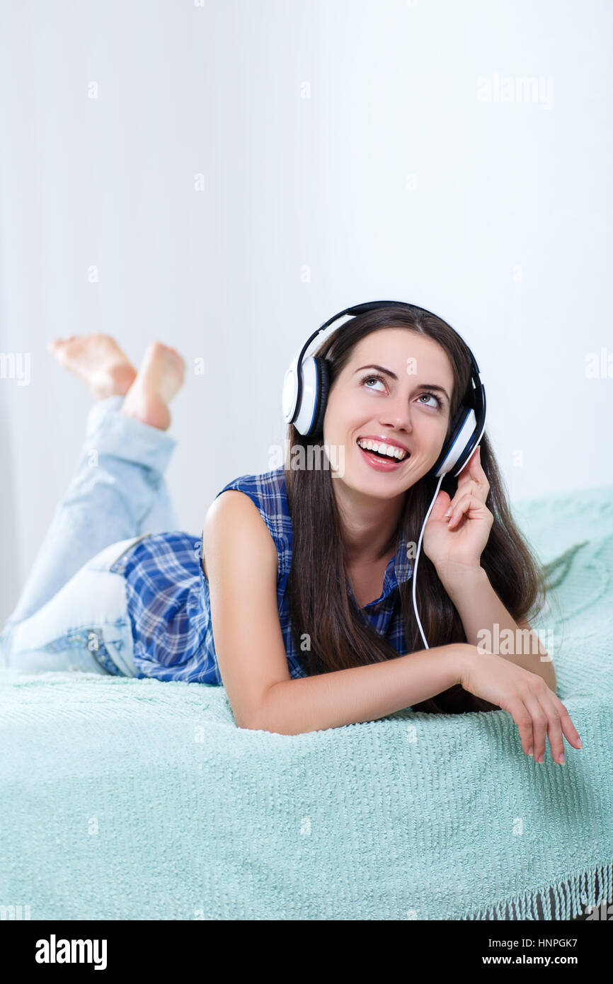 Happy girl listening music using headphones and singing on bed at home. People, leisure and technology concept - happy woman or teenage girl in headph Stock Photo