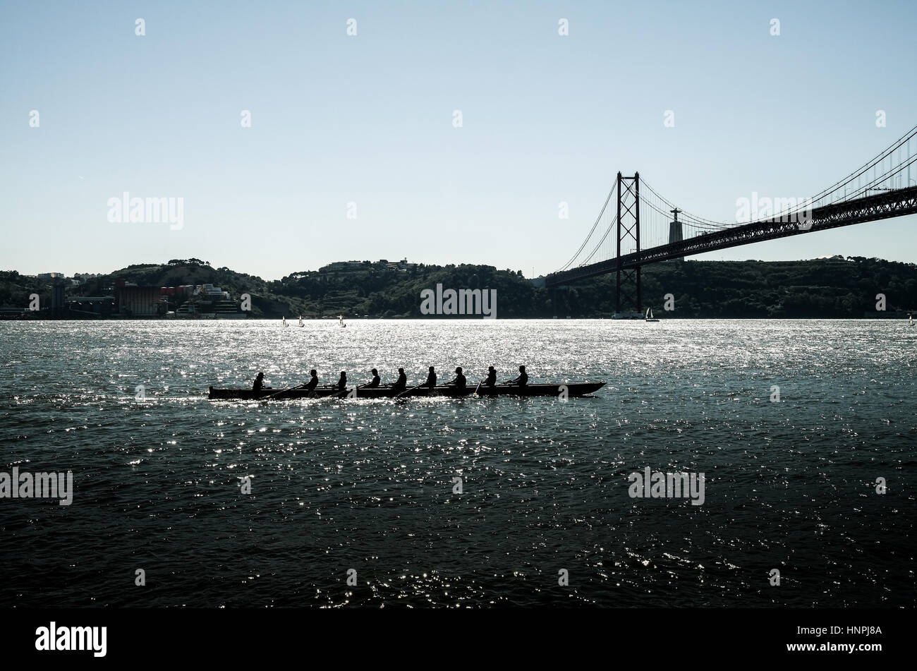 silhouette of people on rowing boat on the sea with suspension bridge in the background. Lisbon, Portugal. Stock Photo