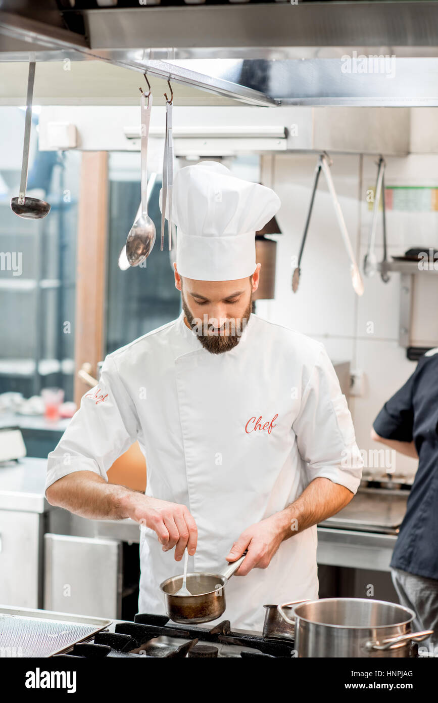 Handsome chef cook in uniform cooking food on the gas stove at the