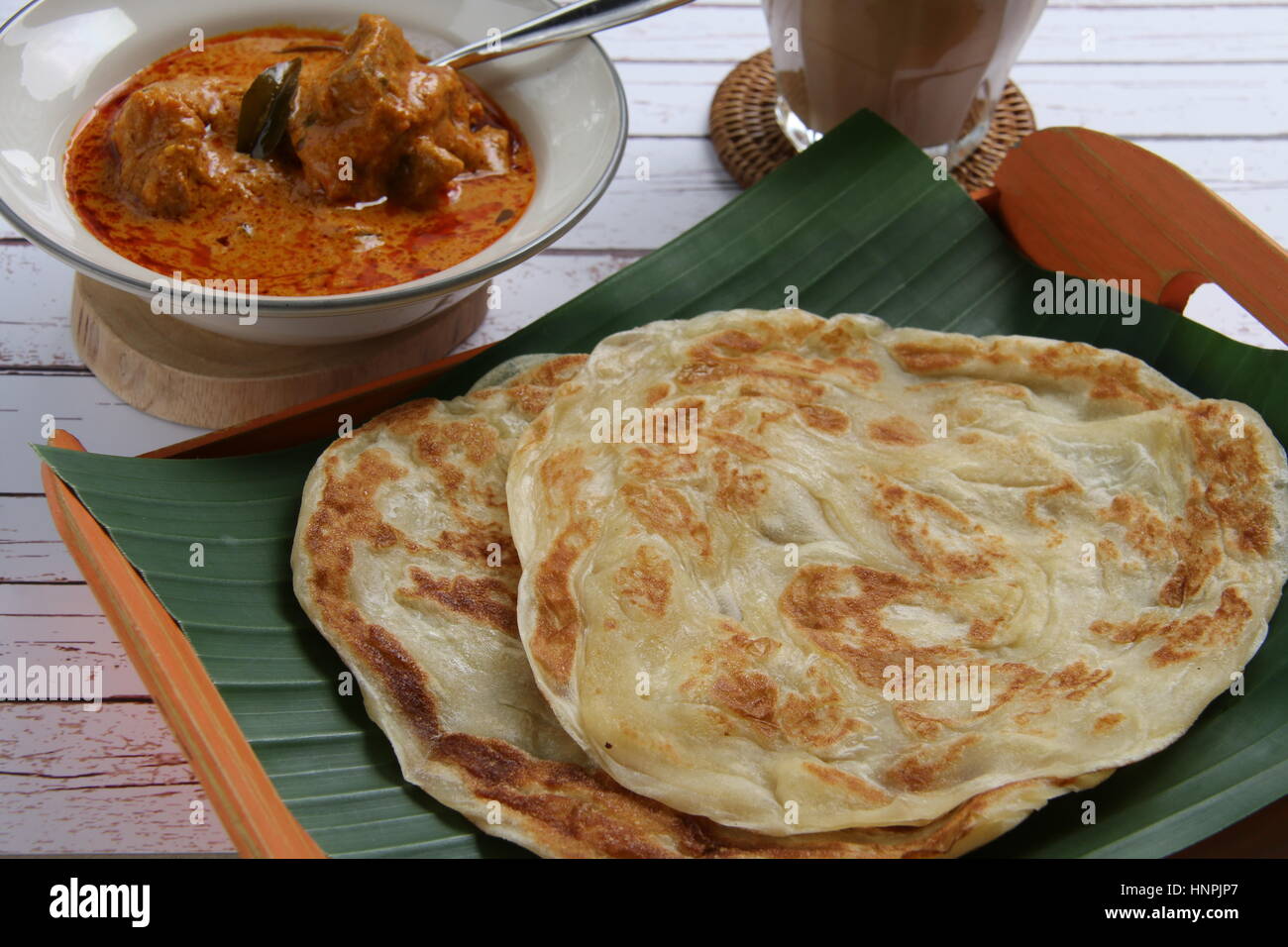 Roti Prata. Indian-influenced flatbread. Plated on a banana-leaf-lined bamboo tray with the chicken curry served separately on a ceramic bowl. Stock Photo
