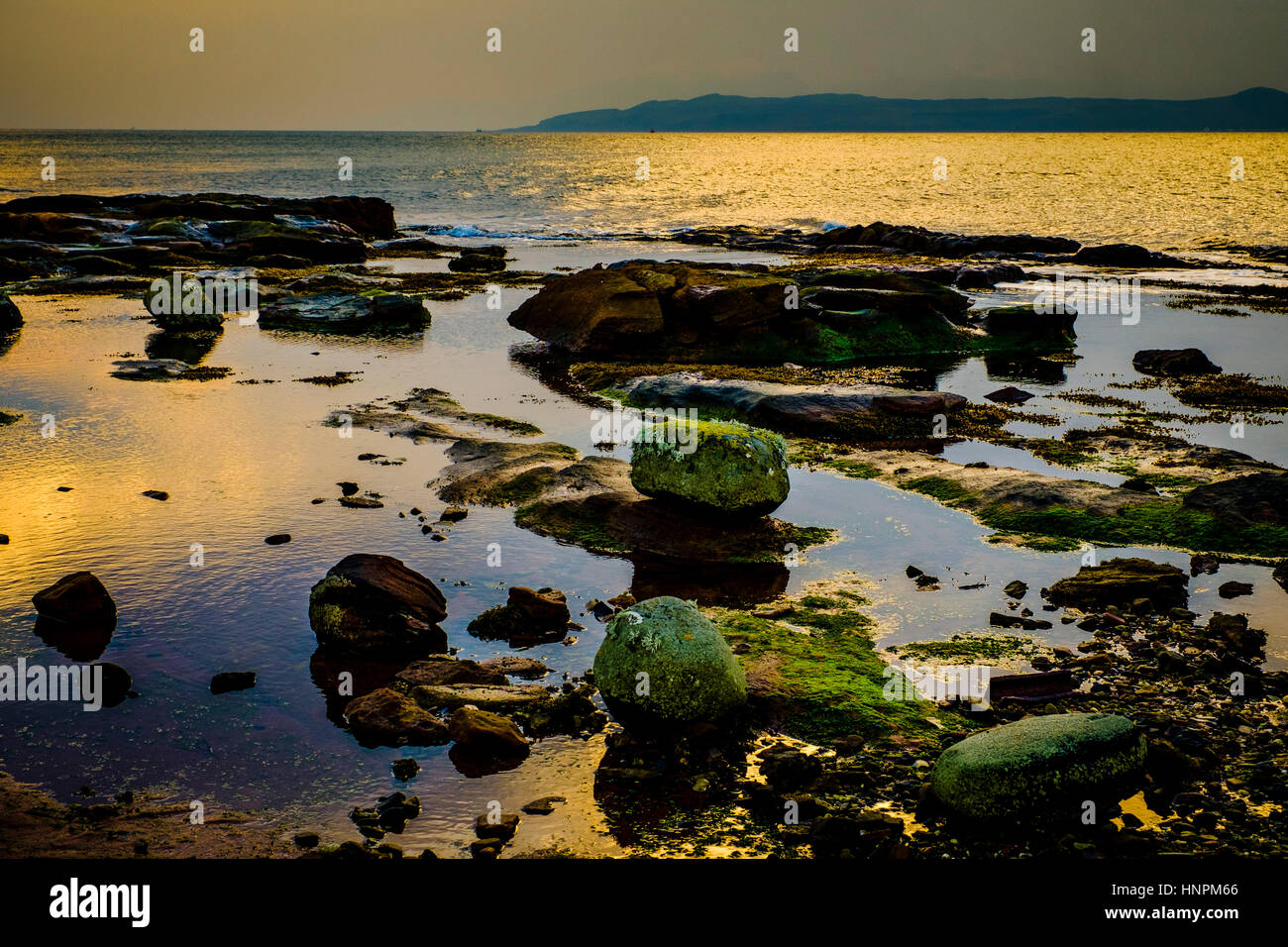 Evening light on the rocks at Little Skate Bay on the west coast of the island of Great Cumbrae, Scotland.  The Isle of Bute can be seen in the backgr Stock Photo