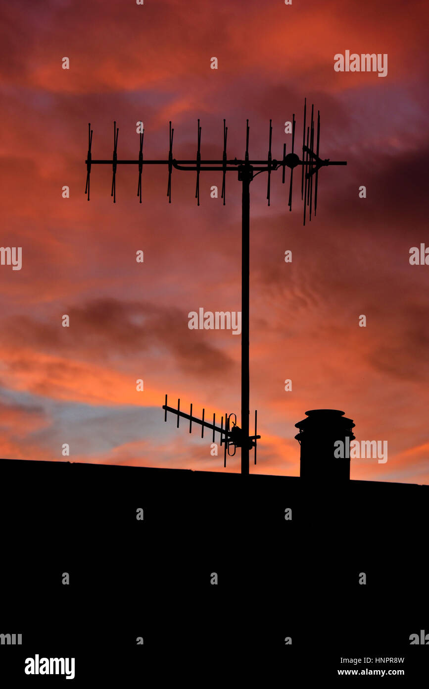 Television aerials and chimney on house roof with sunset sky. Kendal