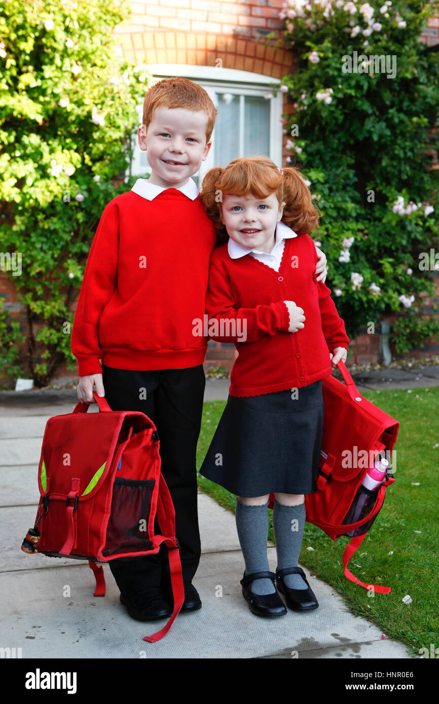 A 4 year old girl with ginger hair on her first day of school, with 7 year old brother. Both in school uniforms. Stock Photo