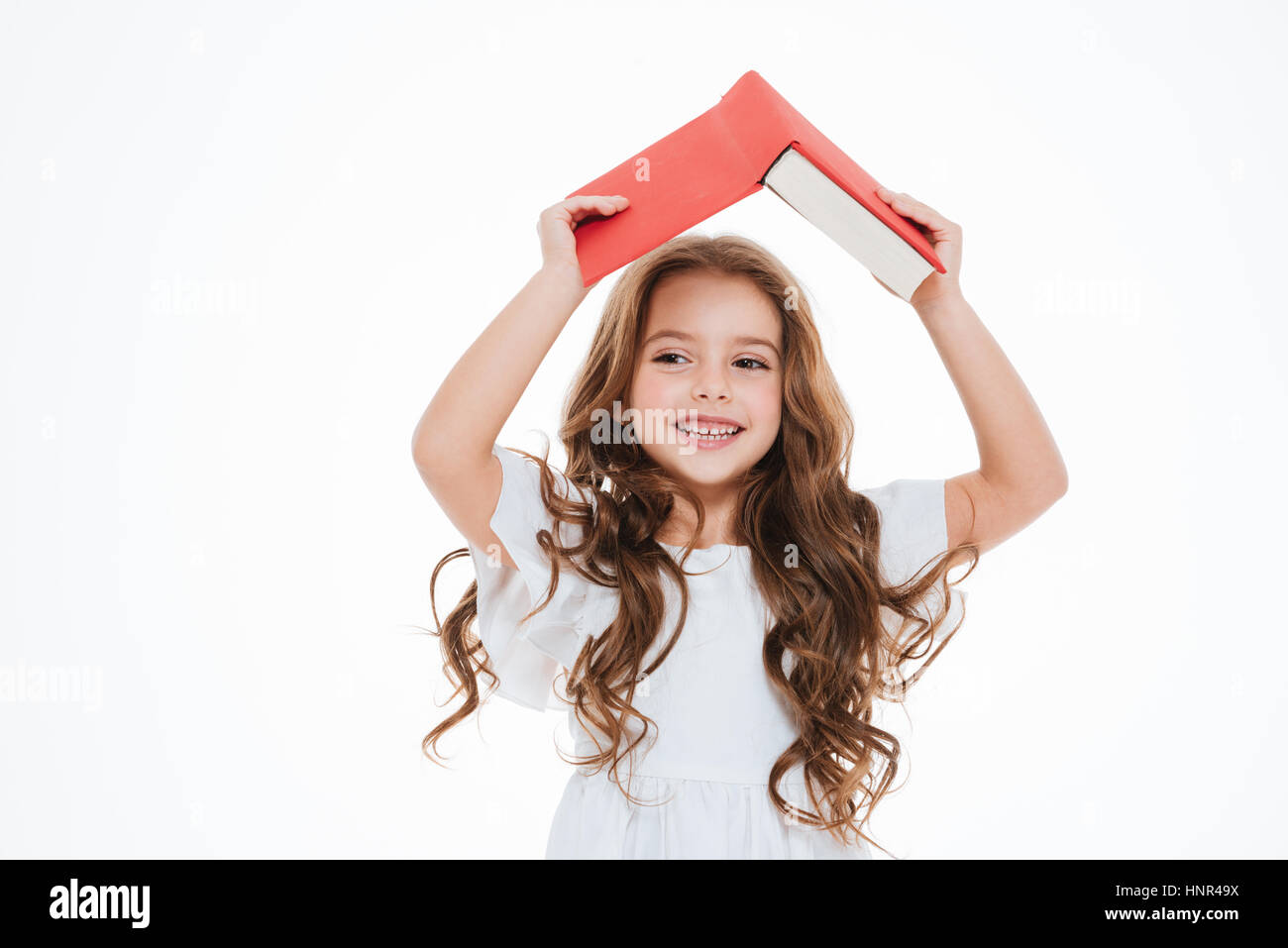 Cheerful little girl holding book above her head over white background ...
