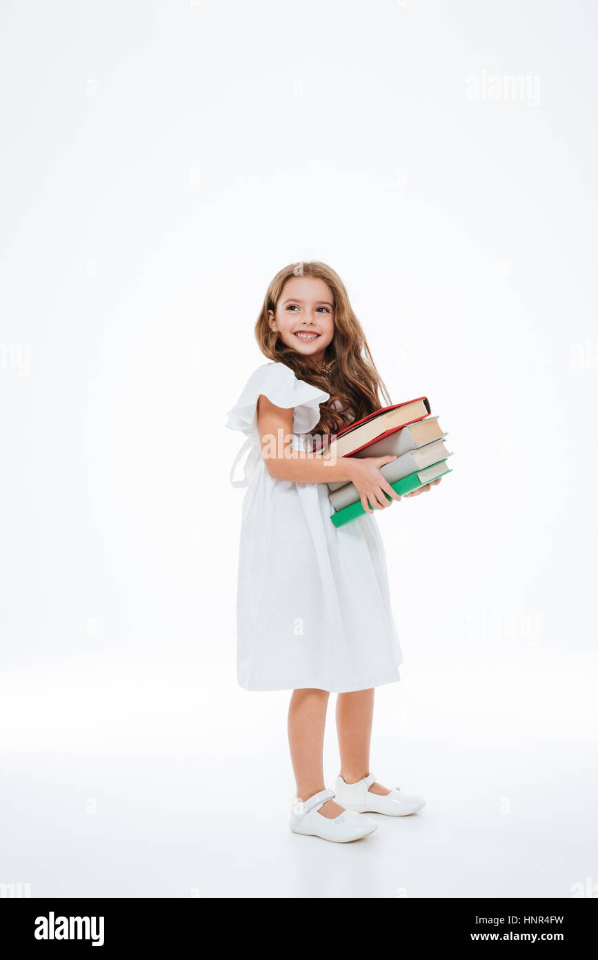 Full length of smiling little girl standing and holding stack of books ...