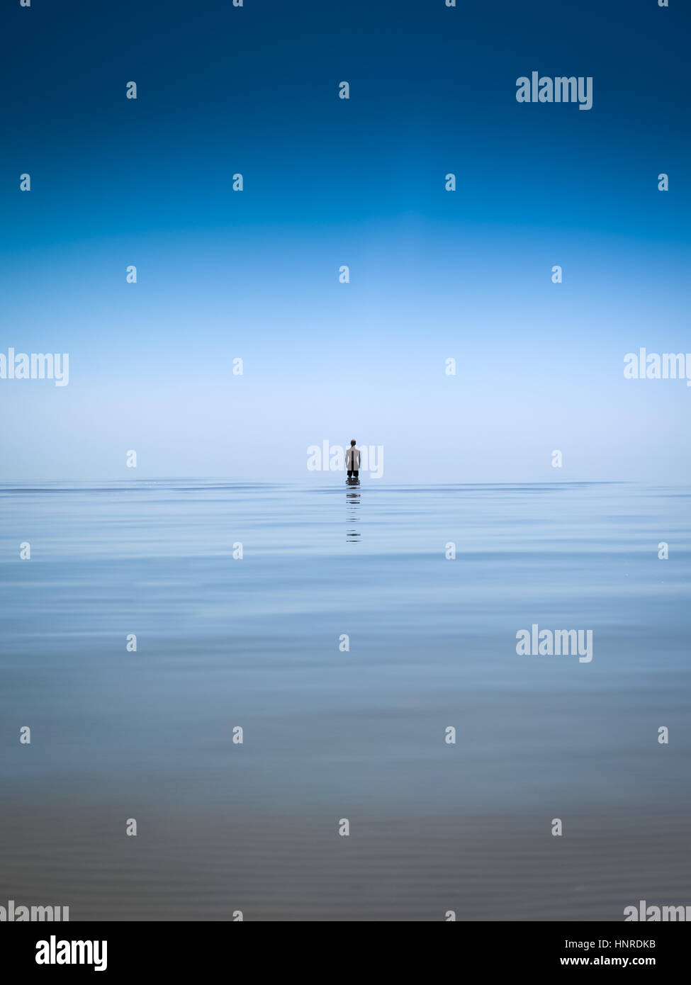 Teenage boy standing alone knee deep in endless still water. Stock Photo