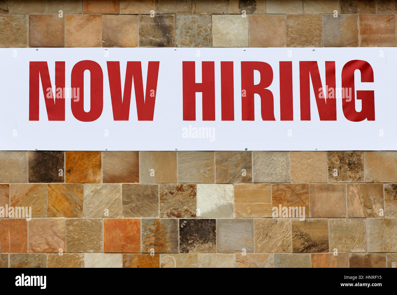 NOW HIRING sign on tiled wall. Stock Photo