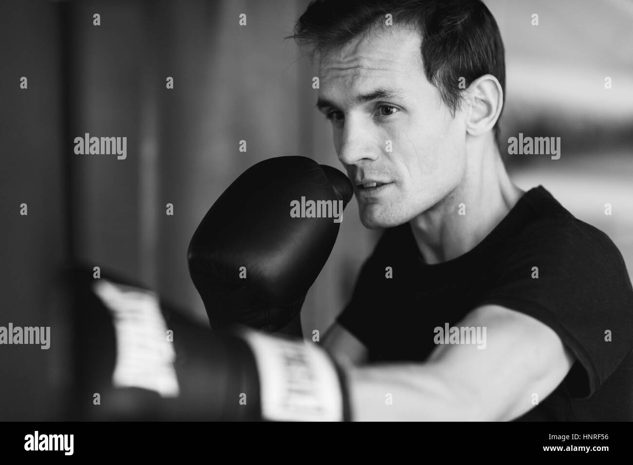 Black-white photo of young boxer near punching bag in gym Stock Photo