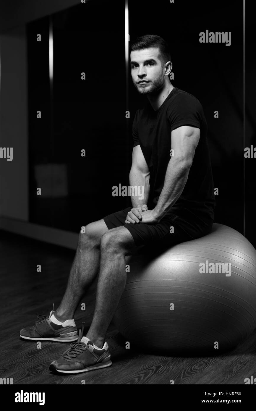 Young athlete sits on fitball at sports center, black and white photo Stock Photo
