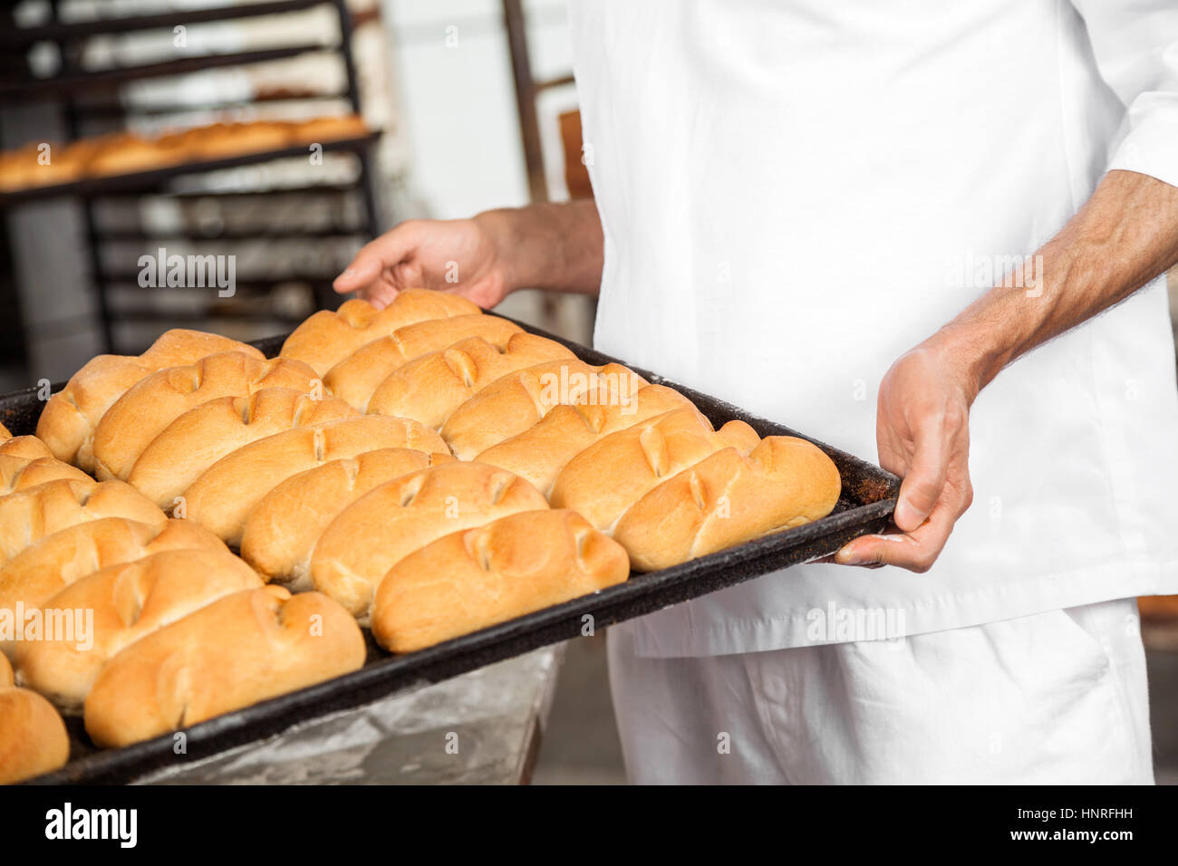 Midsection Of Baker Carrying Breads In Baking Tray Stock Photo