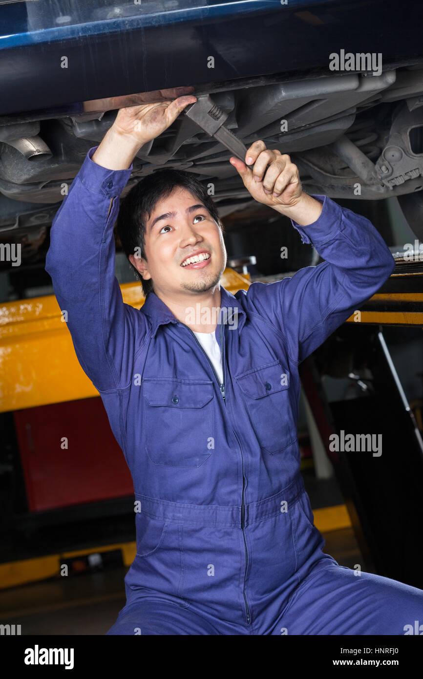 Smiling Mechanic Repairing Underneath Lifted Car Stock Photo