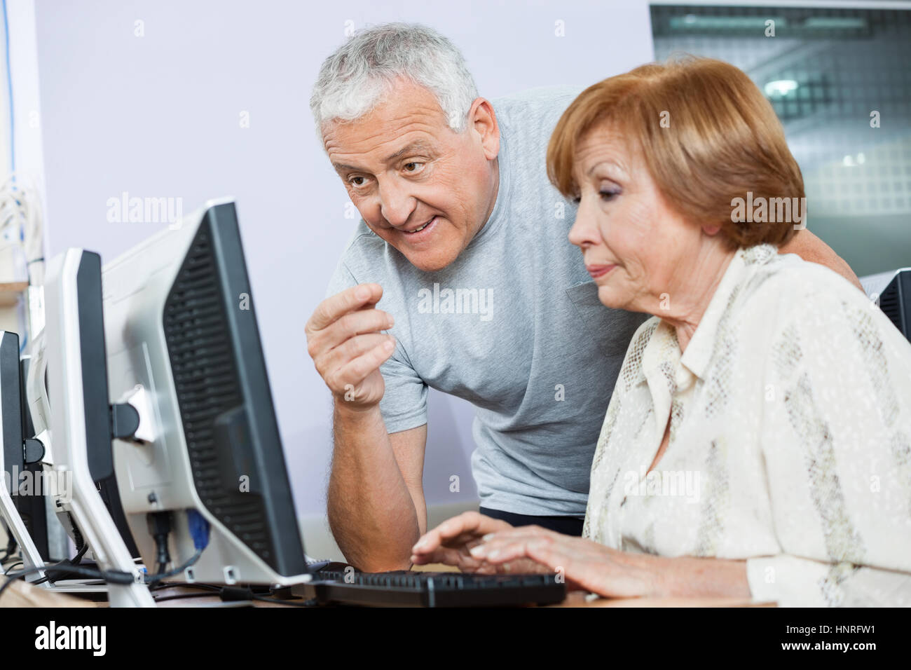 Senior Man Assisting Woman In Computer Class Stock Photo