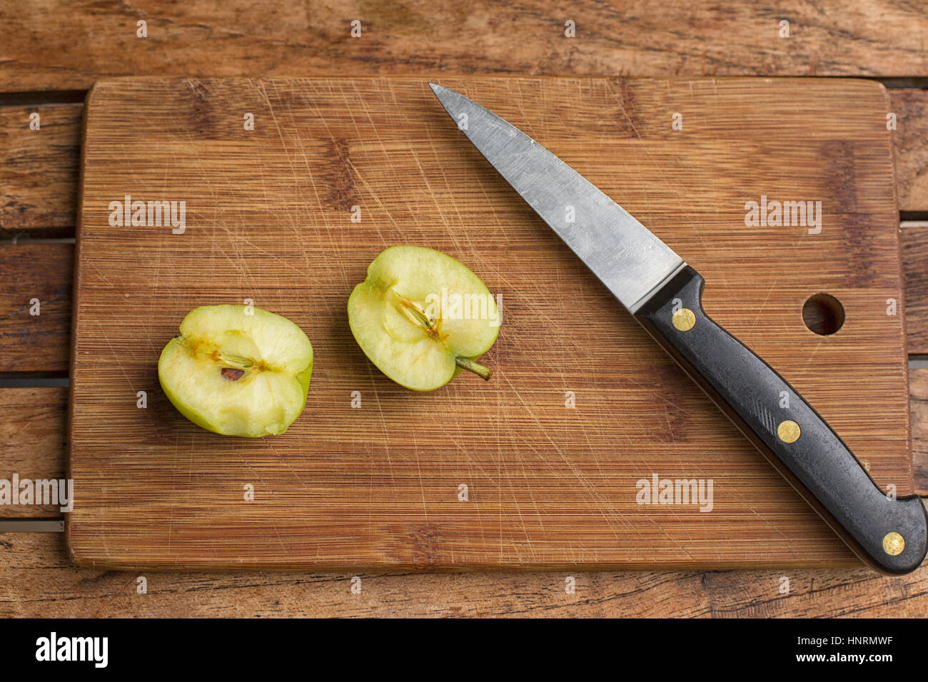 Two halves of an apple and a chef's knife on a wooden cutting board Stock Photo