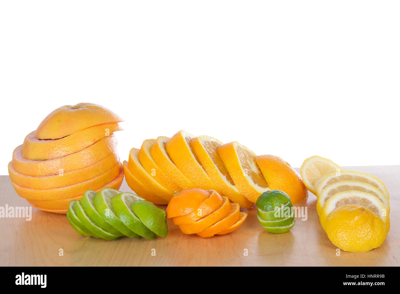 Colorful sliced citrus lined up in stacks on light brown wood table ...