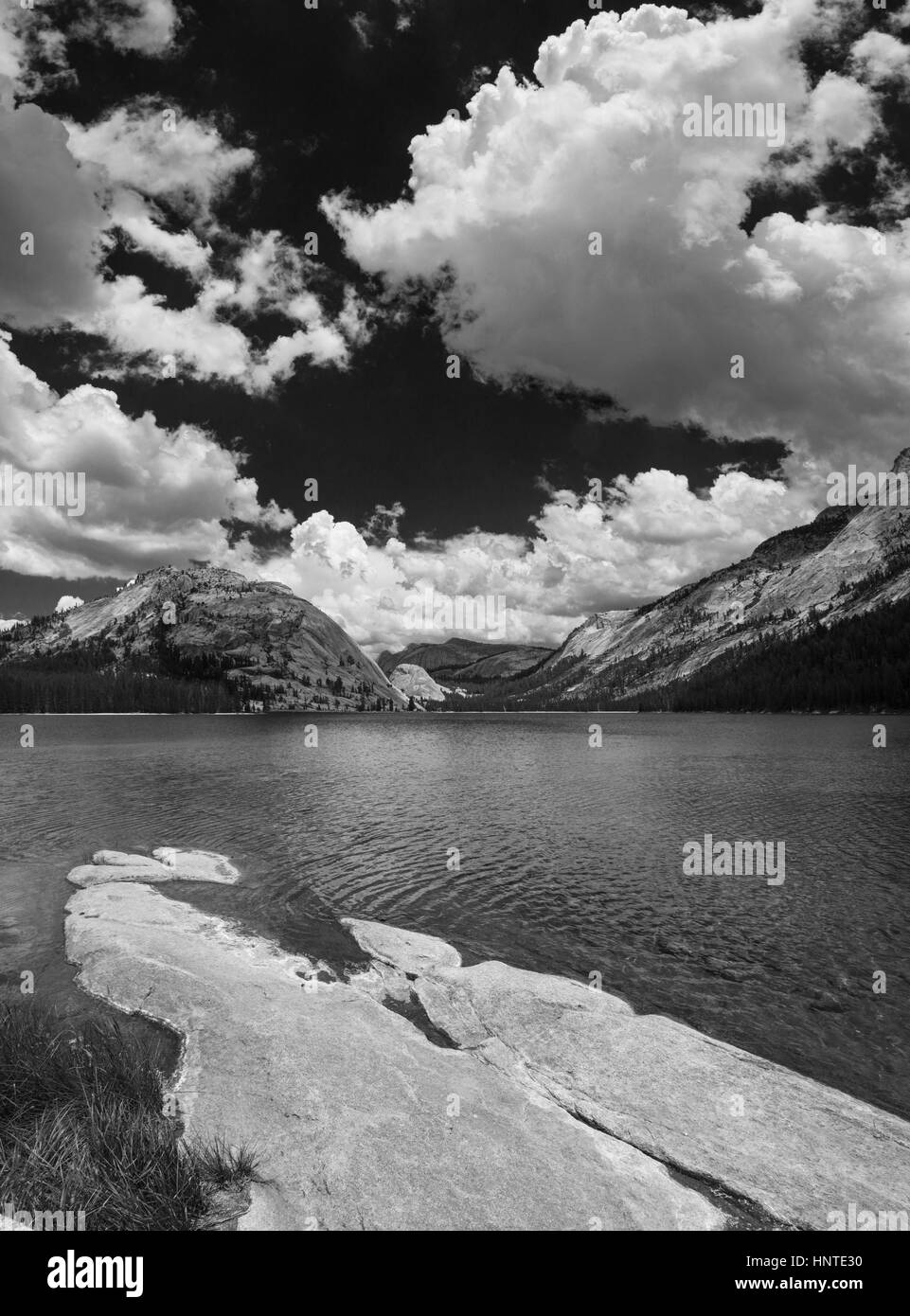 black and white image of Tenaya Lake in the Yosemite National Park high country with foreground rock slab and white clouds in the sky Stock Photo