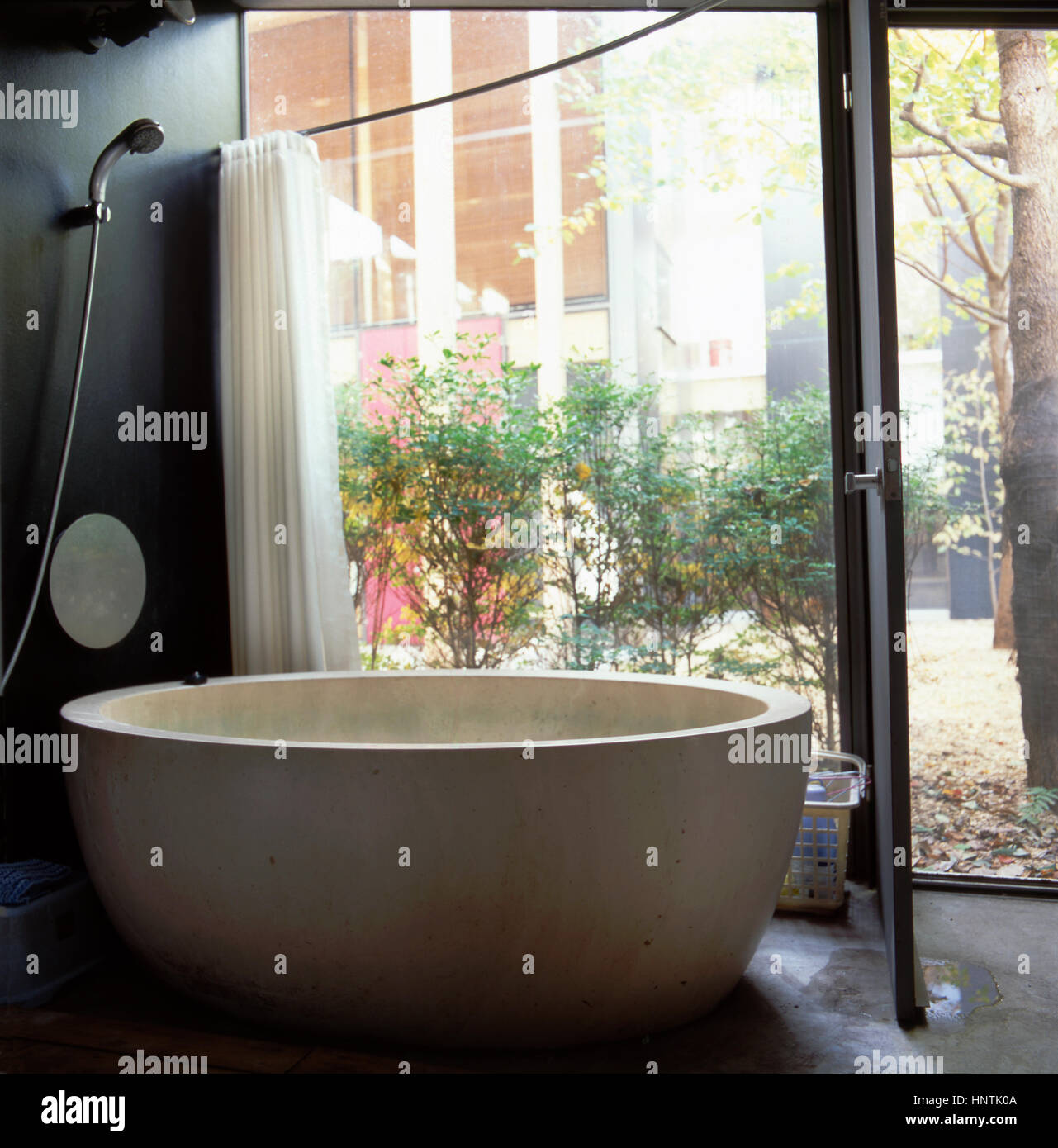Interior of a contemporaneous bathroom with a door facing a private garden  with a big bath tub in japanese house in Tokyo, Japan Stock Photo