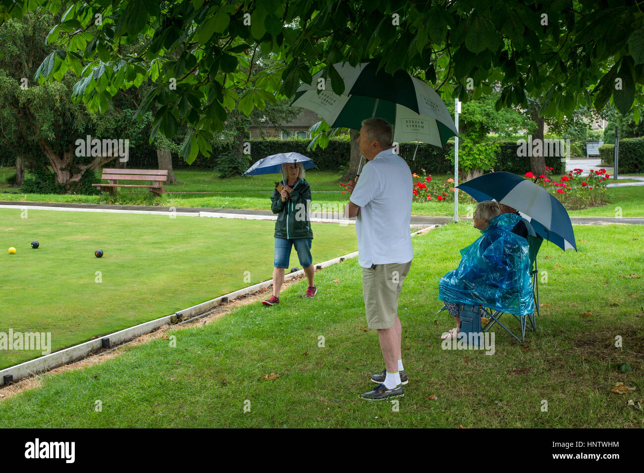 Spectators, with umbrellas, shelter from the rain at a crown green bowling match - village bowling green, Burley In Wharfedale, West Yorkshire, GB. Stock Photo