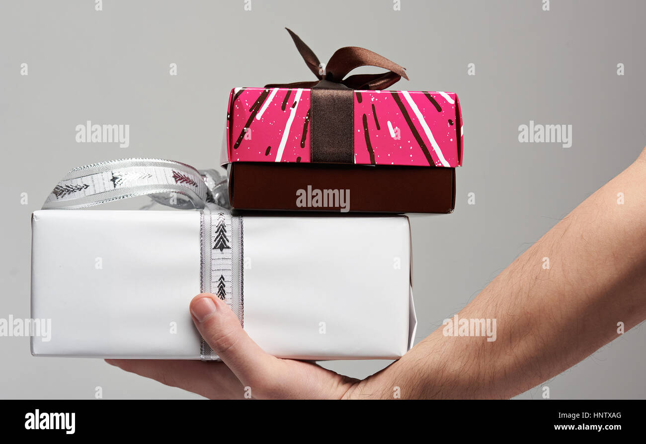 Hand hold colorful boxes with brown ribbon on gray background side view