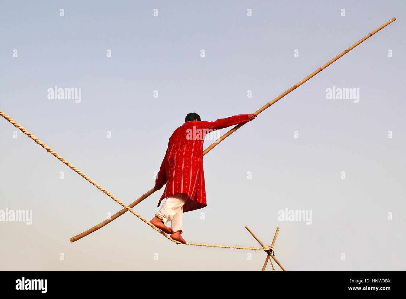 A man doing rope balancing holding a bamboo, wearing red and white clothes Stock Photo