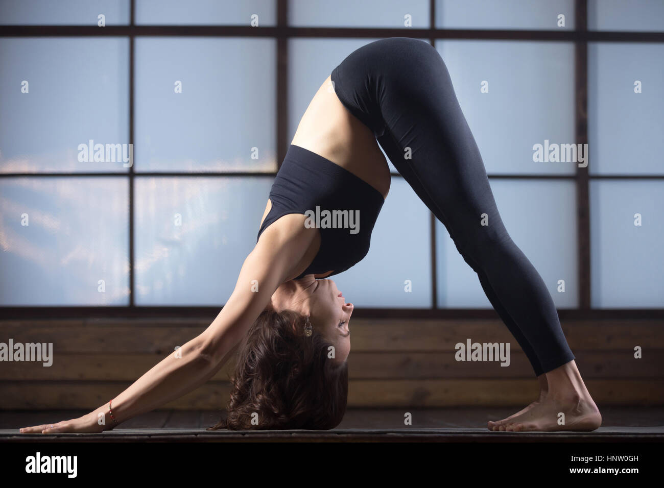 Young woman in adho mukha svanasana pose, studio evening practic Stock Photo