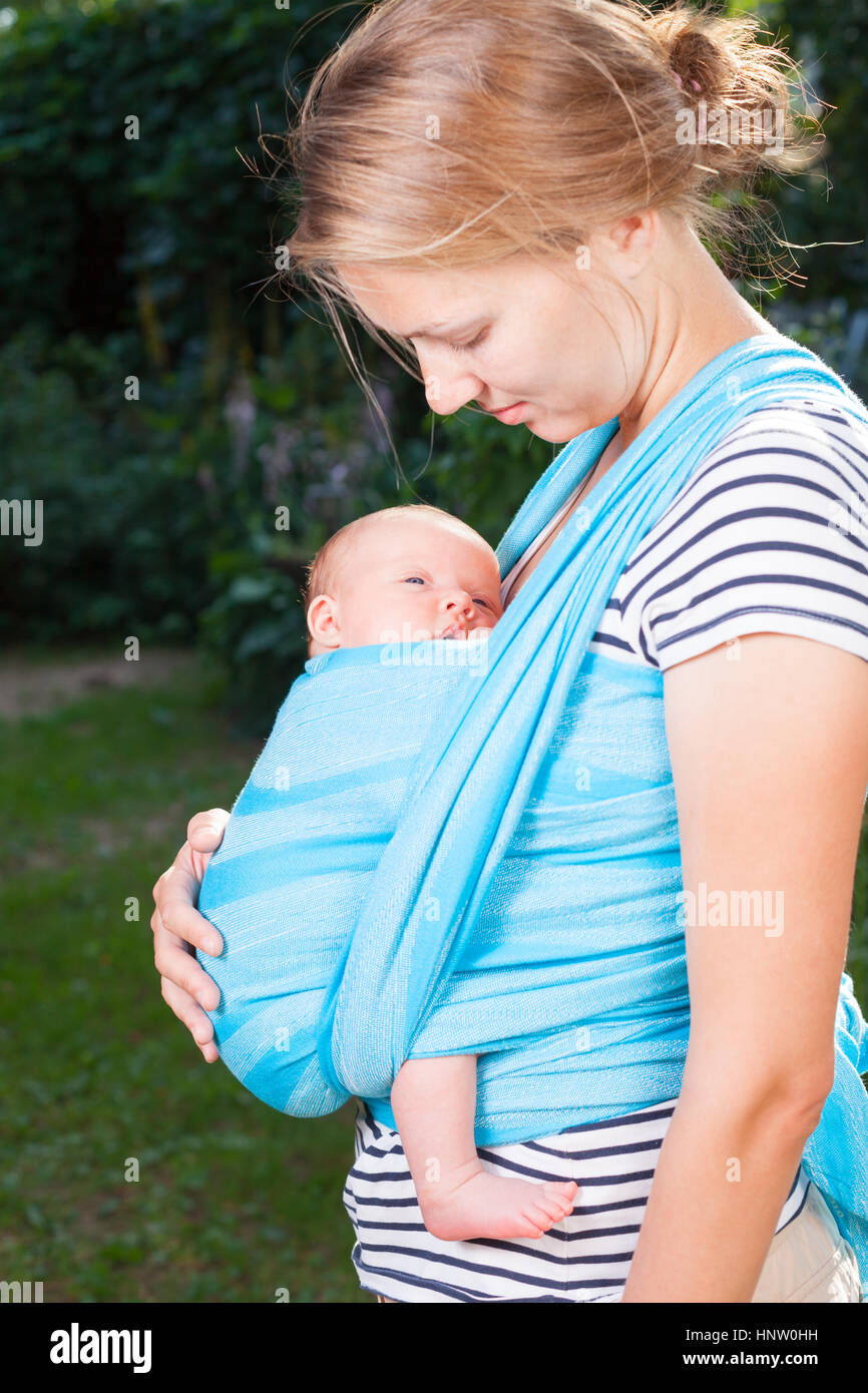 Young mother carrying her little baby girl in blue sling Stock Photo
