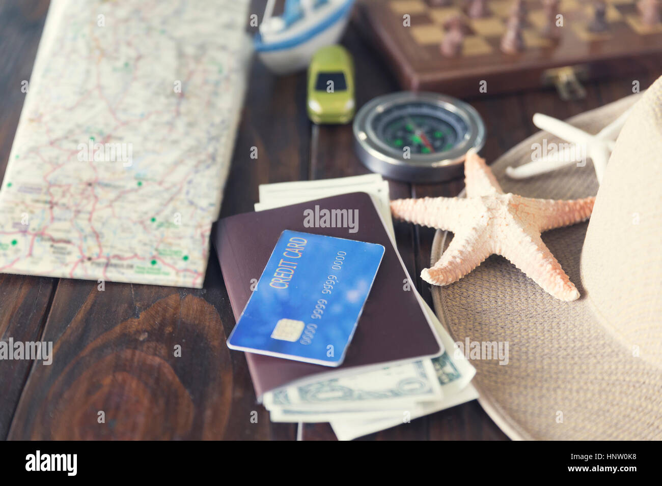 map, chessboard, hat, compass, passport, credit card, banknote money, car ship and starfish figurine on wooden table for use as traveling concept (vin Stock Photo
