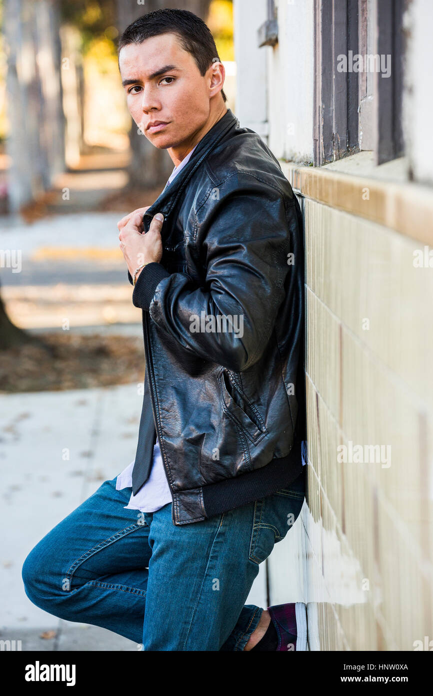 Serious Mixed Race man leaning on wall wearing leather jacket Stock Photo