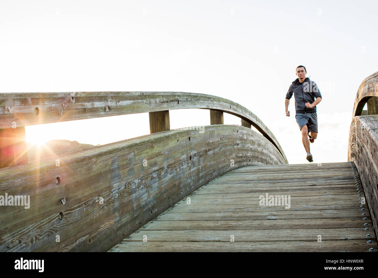 Mixed Race man running at top of curving footbridge Stock Photo