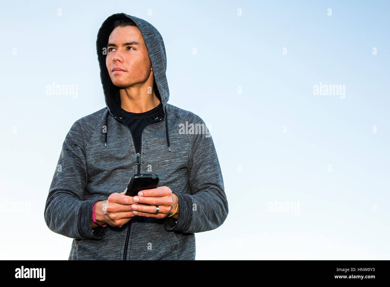 Mixed Race man wearing hoody texting on cell phone Stock Photo