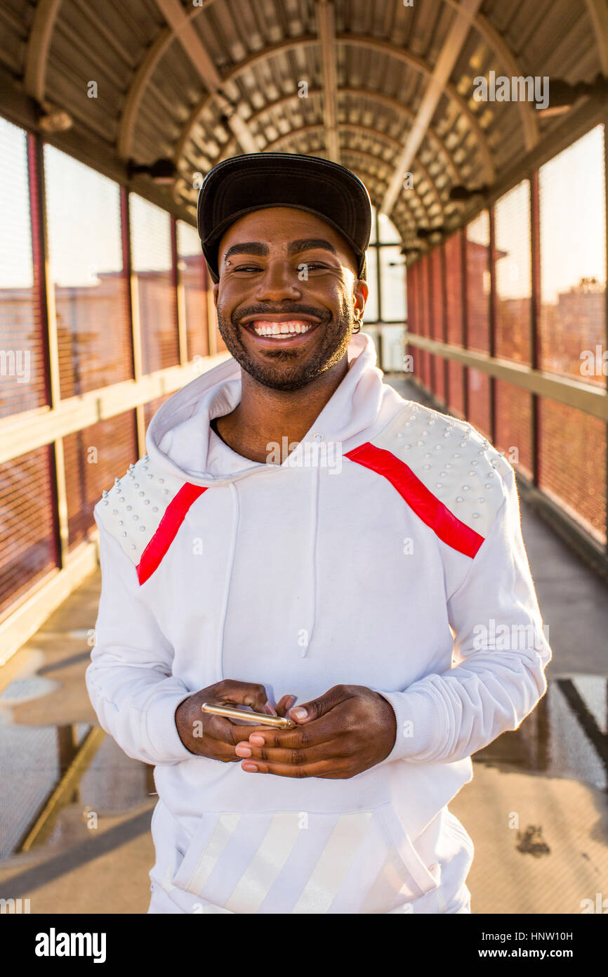 Smiling Black man holding cell phone on footbridge Stock Photo